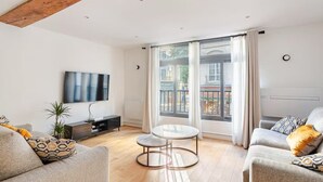 Ein modernes Wohnzimmer mit Flachbildfernseher, rundem Couchtisch und zwei Sofas mit gemusterten Kissen.