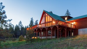 A large wooden cabin with a balcony, surrounded by trees.
