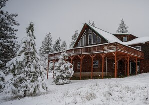 Une grande maison en bois dotée d’un porche, entourée d’arbres couverts de neige.