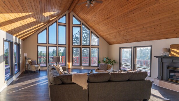 A spacious living room with a high ceiling, large windows, a fireplace, and a cozy seating area.