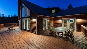 A wooden deck with a dining table and chairs, large windows, and a covered patio area.