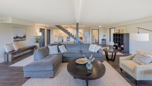 A spacious living room with a grey sectional sofa, a coffee table, and a bookshelf.