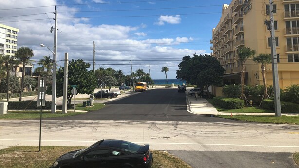 Une rue avec un autobus jaune, des palmiers et un immeuble doté de balcons.