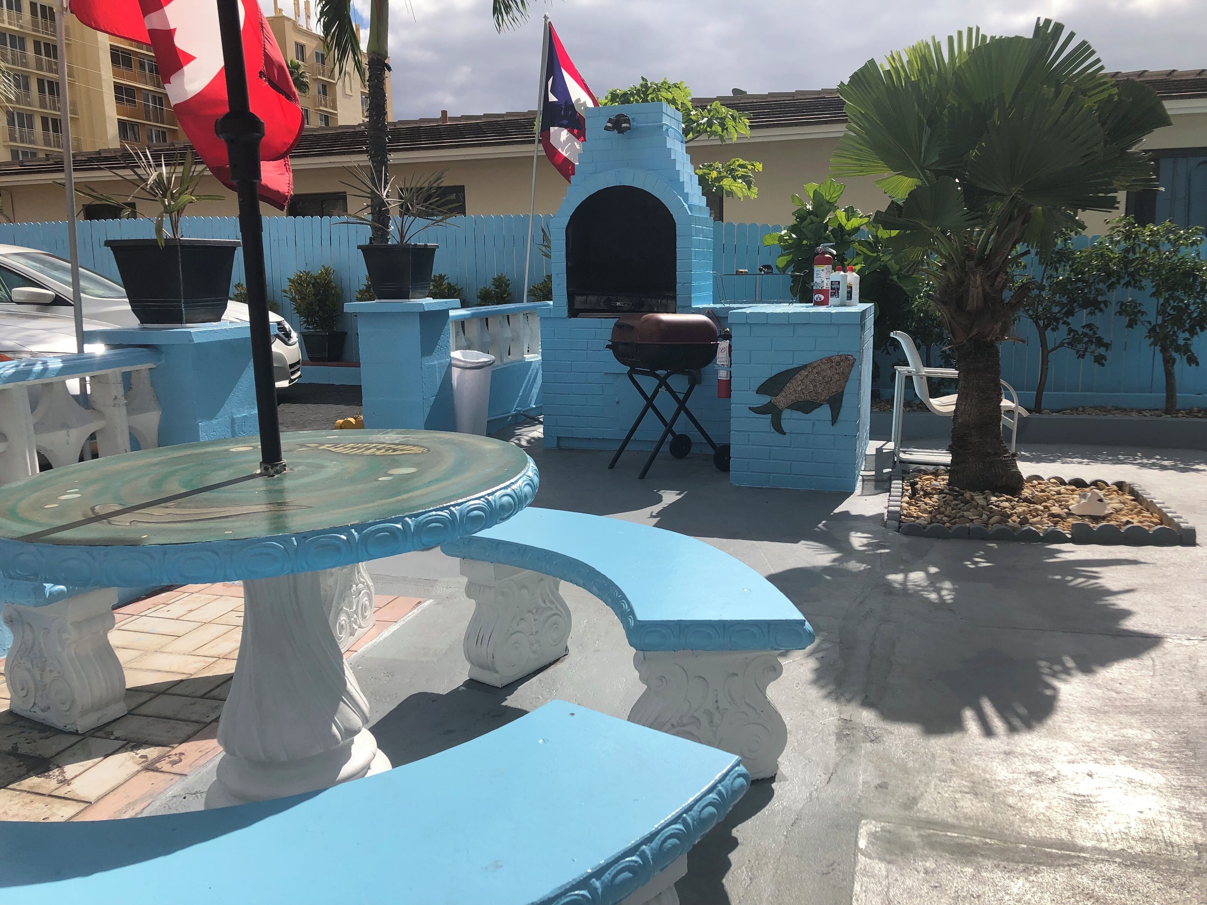 Eine Terrasse mit blauer Wand, Grill, Zierteich und einer Flagge.
