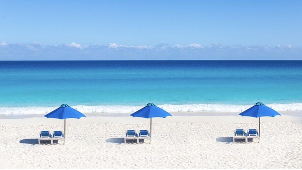 A beach with three blue umbrellas and two white lounge chairs. - Luxury Villa at the feet of the sea In Cancun (Cancún)