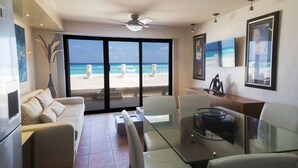 A modern living room with a glass table, white sofa, and a view of the beach. - Luxury Villa at the feet of the sea In Cancun (Cancún)