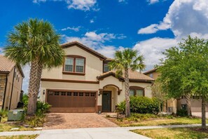 A two-story house with a garage, surrounded by palm trees and a clear blue sky. - Magical Theme Rooms, Water Park, Arcade, Sleep 18! 15 mins to Disney (Kissimmee)