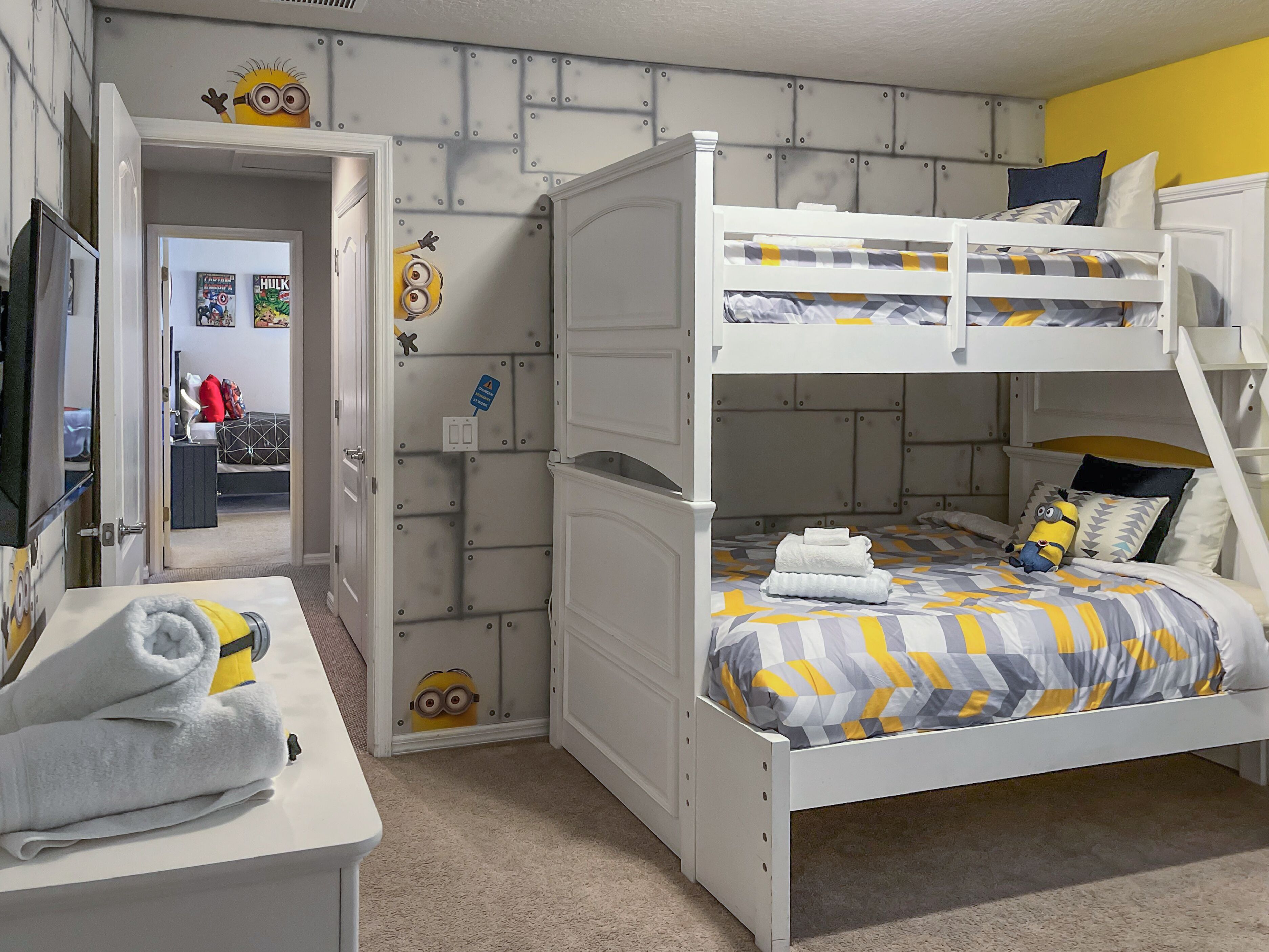Une chambre avec un lit superposé doté d’une tête de lit blanche, un bureau avec une chaise et une porte donnant sur une autre pièce.