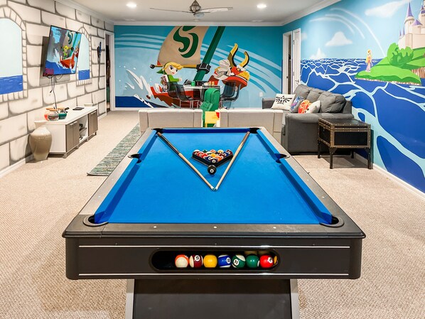 A pool table in a room with a mural of a sailing scene, a sofa, and a television. - Magical Theme Rooms, Water Park, Arcade, Sleep 18! 15 mins to Disney (Kissimmee)