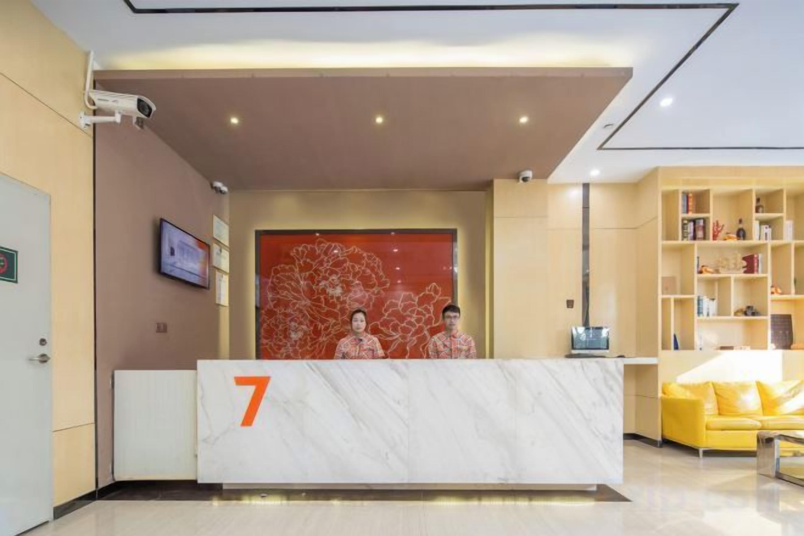 A hotel reception area with a marble reception desk marked with the number 7, a yellow sofa, and a bookshelf.