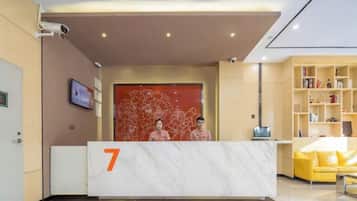 A hotel reception area with a marble reception desk marked with the number 7, a yellow sofa, and a bookshelf.