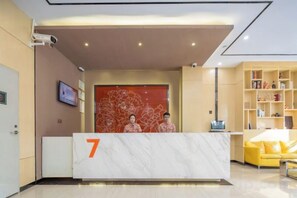 A hotel reception area with a marble reception desk marked with the number 7, a yellow sofa, and a bookshelf. - 7 Days Premiuml (Shenzhen Longgang Universiade Center Ailian subway station) (Shenzhen)