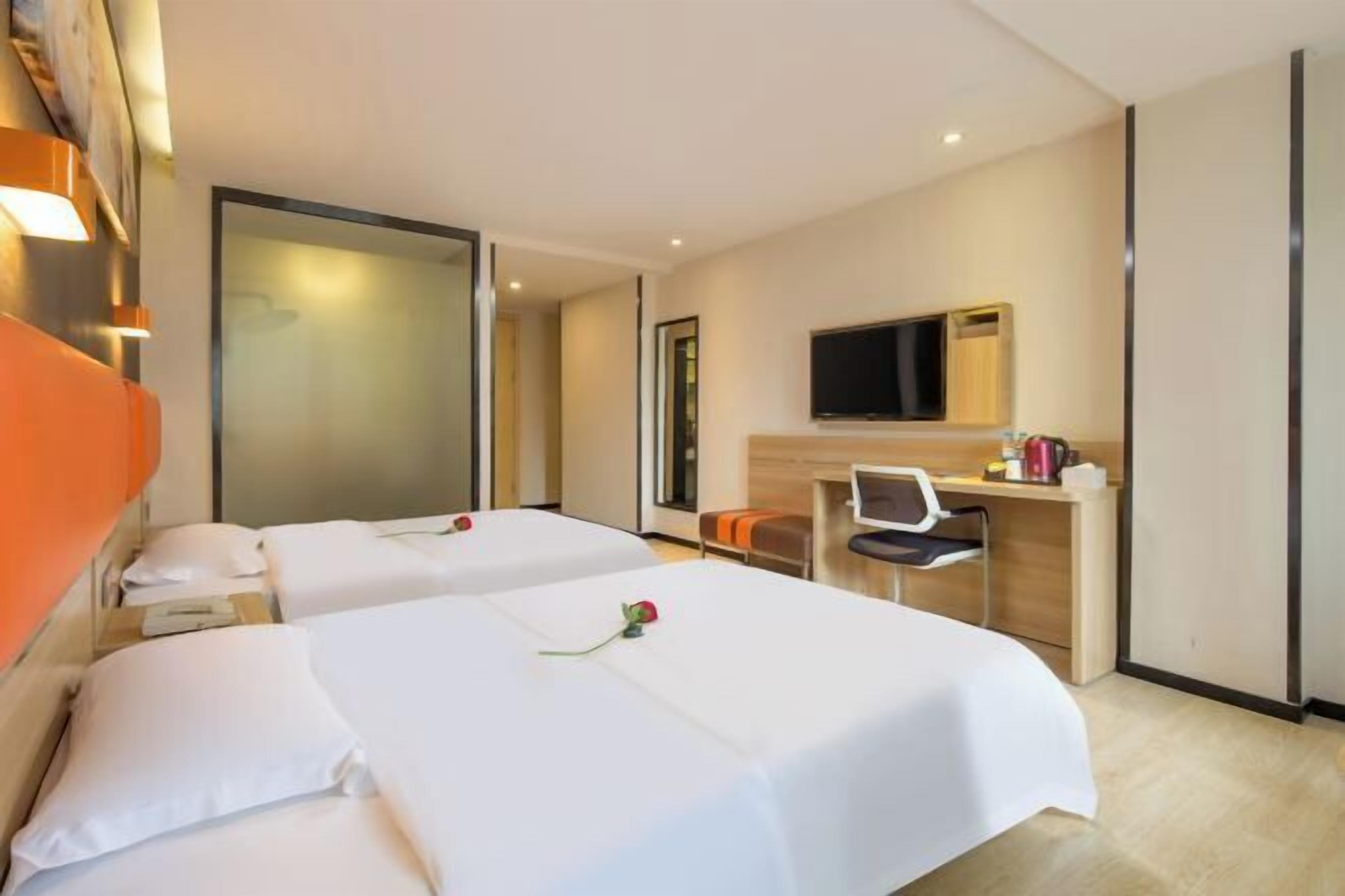 A hotel room with two beds, a desk, a chair, a television, and a large mirror.