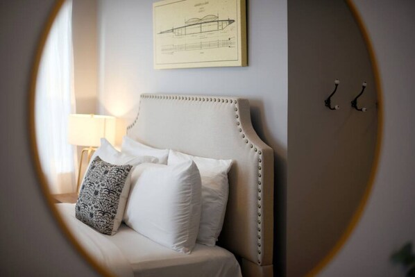 A bed with white bedding and a patterned pillow, a lamp, and a framed architectural drawing on the wall.
