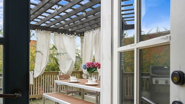 An outdoor deck with a wooden table and chairs, a pergola with white curtains, and a view of the surrounding garden. - ★Farmhouse Style★Outdoor Patios★Parking!★Beautiful (Pittsburgh)