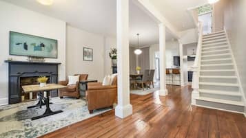 A spacious living room with hardwood flooring, a fireplace, a dining area, and a staircase.