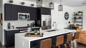 A modern kitchen with dark cabinetry, a white island with bar stools, stainless steel appliances, and pendant lighting. - Brand new property with hot tub, fire pit, parking, covered ski storage, and more! (Silverthorne)