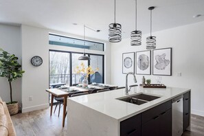 A modern kitchen with a large island, pendant lights, and artwork on the wall. - Brand new property with hot tub, fire pit, parking, covered ski storage, and more! (Silverthorne)