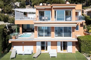 Ett modernt hus i två våningar med en swimmingpool, utomhusmöbler och stora fönster.