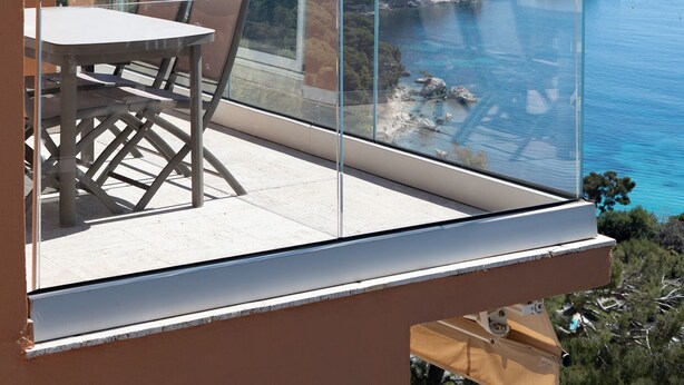 Un balcone con tavolo e sedie, affacciato su un paesaggio costiero sotto un cielo sereno.