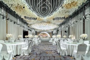 A banquet hall with round tables, white chairs, and a chandelier.