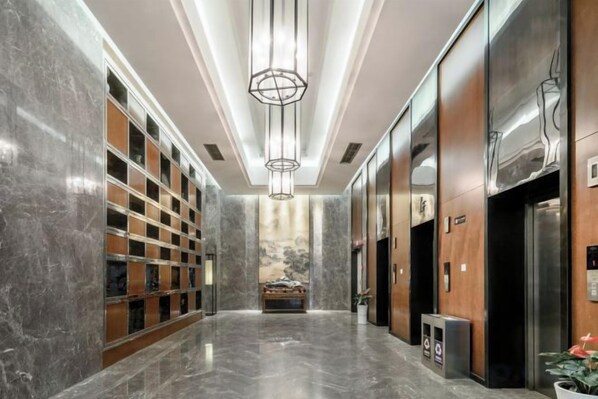 A modern hotel lobby with marble floors, a central chandelier, and a reception desk.