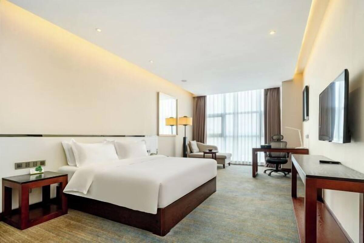 A hotel room with a large bed, a desk, a chair, a TV, and a window with curtains.