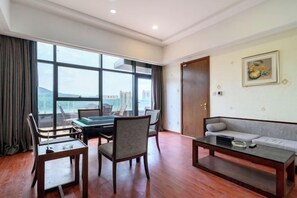 A room with a dining table, chairs, a sofa, and a large window offering a view of buildings.