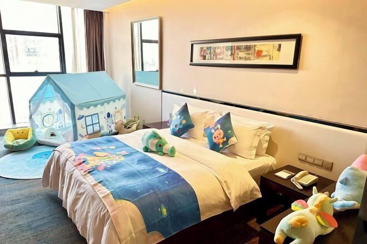 A hotel room with a bed, a desk, a chair, a window, and a wall-mounted picture.