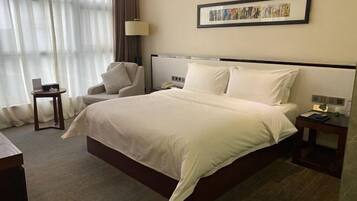 A hotel room with a large bed, a chair, a nightstand, a lamp, and a framed picture on the wall.