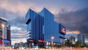 A modern building with a prominent vertical design, large signage, and a busy street with light trails.