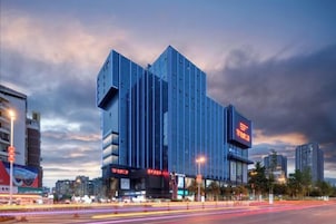 Un edificio moderno con un diseño vertical destacado, señalización grande y una calle concurrida con estelas de luz.
