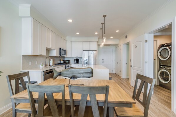 A modern kitchen with white cabinets, a wooden dining table, and a built-in washer and dryer.