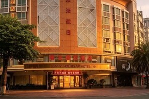 Um hotel com entrada destacada, janelas amplas e uma placa indicando ser o Sunny Holiday Hotel.