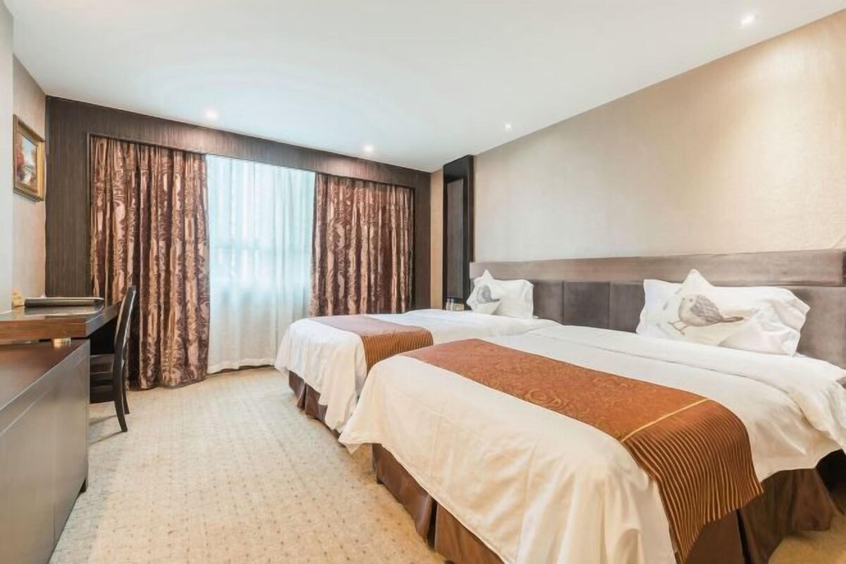A hotel room with two beds, a desk, and a large window with curtains.