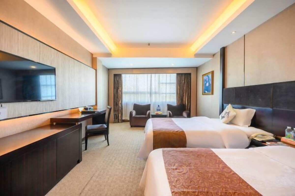 A hotel room with a large bed, a desk, a chair, a television, and a window with curtains.