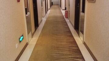 Un pasillo de hotel con suelo alfombrado, puertas a ambos lados y una lámpara en la pared izquierda.