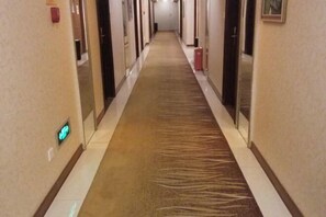 A hotel hallway with a carpeted floor, doors on both sides, and a light fixture on the left wall. - Sunny Holiday Hotel (Shishi)