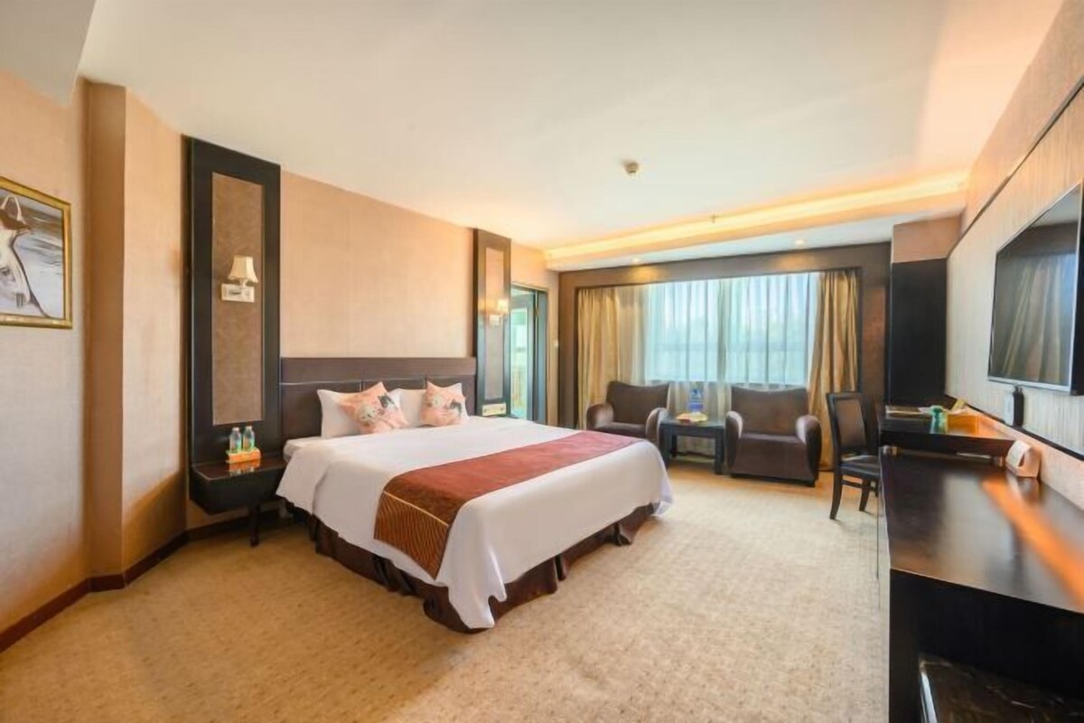 A hotel room with a large bed, a desk, a chair, and a television.