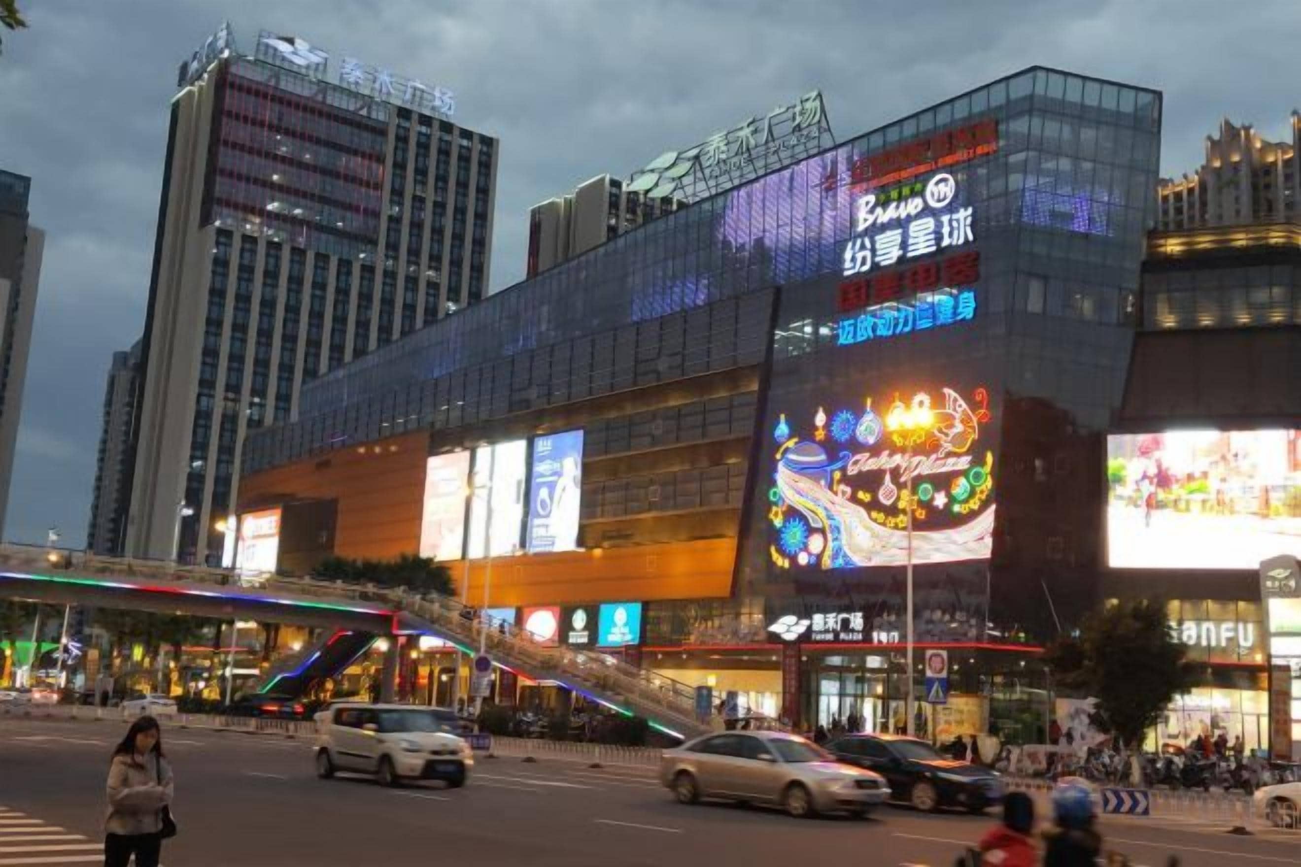 A multi-story commercial building with large digital billboards and a pedestrian overpass.