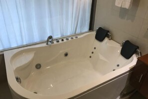 A large, white bathtub with two black bath seats, a window with curtains, and a towel rack on the wall. - Sunny Holiday Hotel (Shishi)
