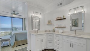 A modern bathroom with white cabinetry, a large mirror, and a ceiling fan.
