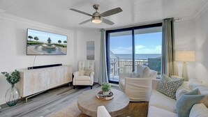 A modern living room with a large window, a ceiling fan, a flat-screen TV, a wooden coffee table, and a white sofa.