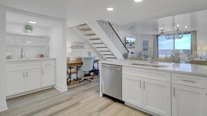 A modern kitchen with white cabinetry, a central island, and a staircase leading to another level.