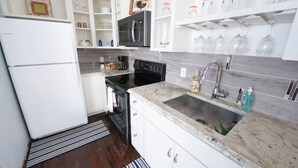 A modern kitchen with white cabinets, a black microwave, a stainless steel refrigerator, and a granite countertop. - Downtown Studio Gem (Nacogdoches)