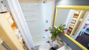 A bathroom with a shower, toilet, sink, and a mirror with a yellow frame. - Downtown Studio Gem (Nacogdoches)