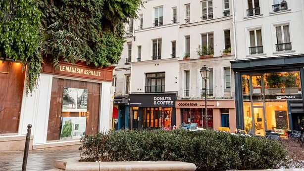 A building with a vertical garden facade, a shop named "Le Magasin Asphalte," and adjacent storefronts including "Donuts & Coffee" and "Living Packets."