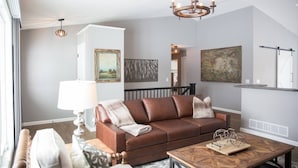 A modern living room with a brown leather sofa, a wooden coffee table, and a chandelier. - Centrally Located 2BR 2BA Home - Garage Parking & Fully Equipped Kitchen/Laundry (Janesville)