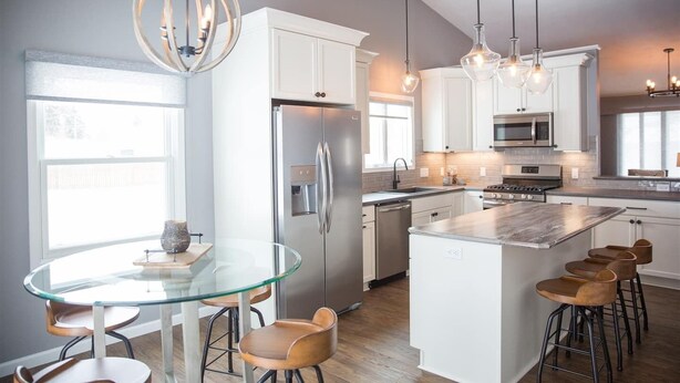 A modern kitchen with white cabinets, stainless steel appliances, a glass dining table, and bar stools. - Centrally Located 2BR 2BA Home - Garage Parking & Fully Equipped Kitchen/Laundry (Janesville)