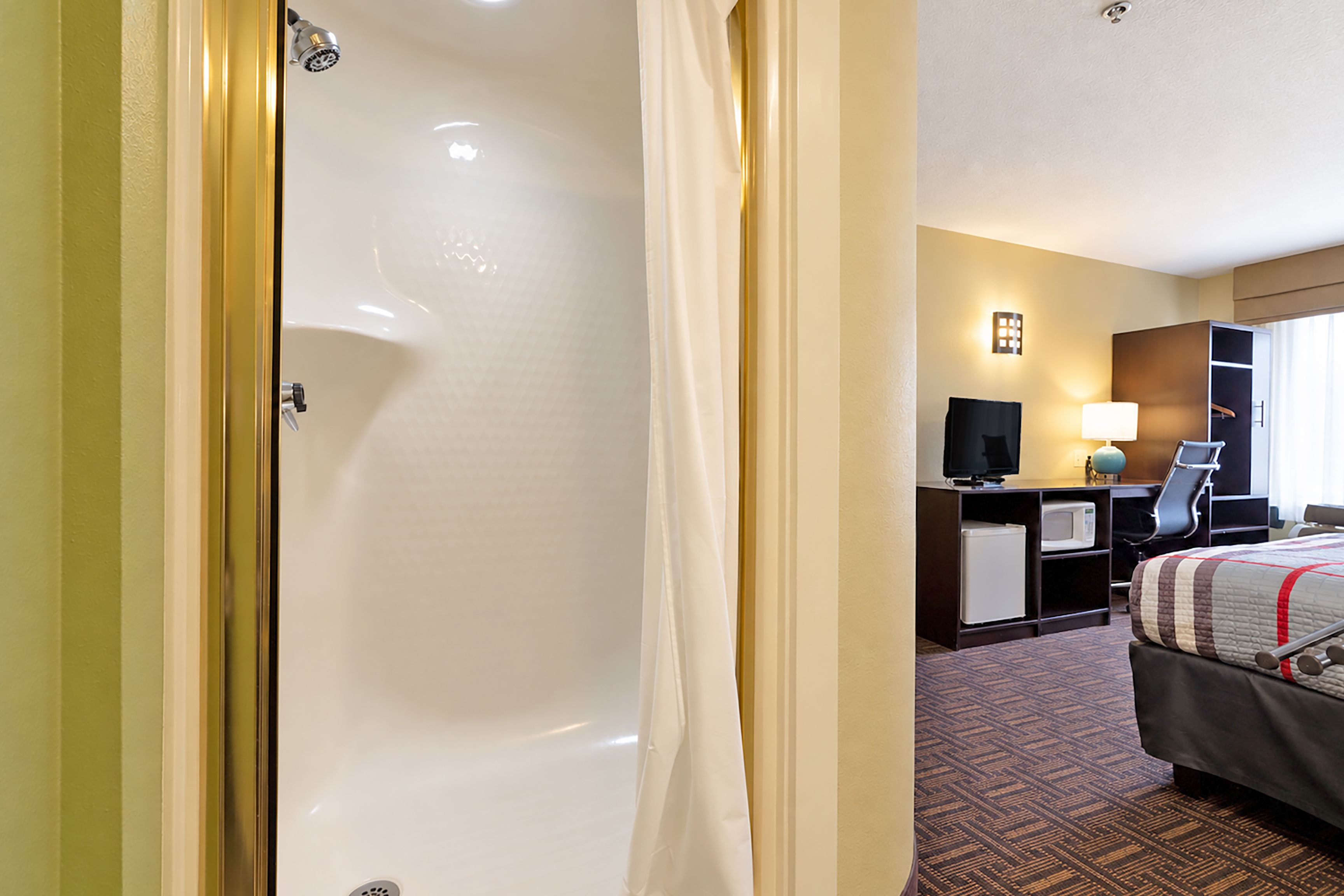 Una camera d'albergo con vasca da bagno, una scrivania con televisore, un letto e una finestra con tende.
